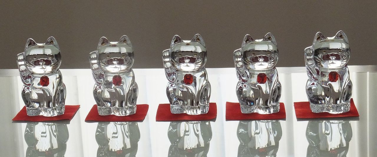 4つのバカラ製タンブラー（アビス、アルマニャック、ローハン、アルルカン）が、モダンなガラステーブルの上に横一列に並んでいる写真。左から、重厚なフラットカットが特徴のアビス、斜めの深いカットが輝くアルマニャック、繊細な蔓草模様のエッチングが施されたローハン、そして色彩豊かな道化師の衣装をイメージしたカットのアルルカンが並び、それぞれのクリスタル特有の輝きとデザインの個性が際立っている。透明なガラステーブルが光を透過させ、各グラスの複雑なパターンと美しい影を美しく映し出し、バカラの多様な芸術性を一堂に感じさせる洗練された光景を表現している。