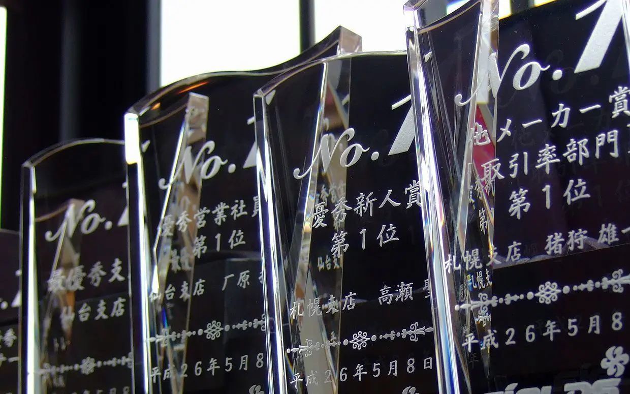 クリスタルトロフィーの正面に、力強い『No.1』の文字と賞名、受賞者氏名、日付、企業名を精緻に名入れ彫刻したサンプル写真。透明度の高いクリスタルが周囲の光を反射し、トップの座に輝いた卓越した功績と栄誉を、現代的でシャープなデザインでダイナミックに称える、最高級の法人向け年間表彰・MVP記念のイメージ。