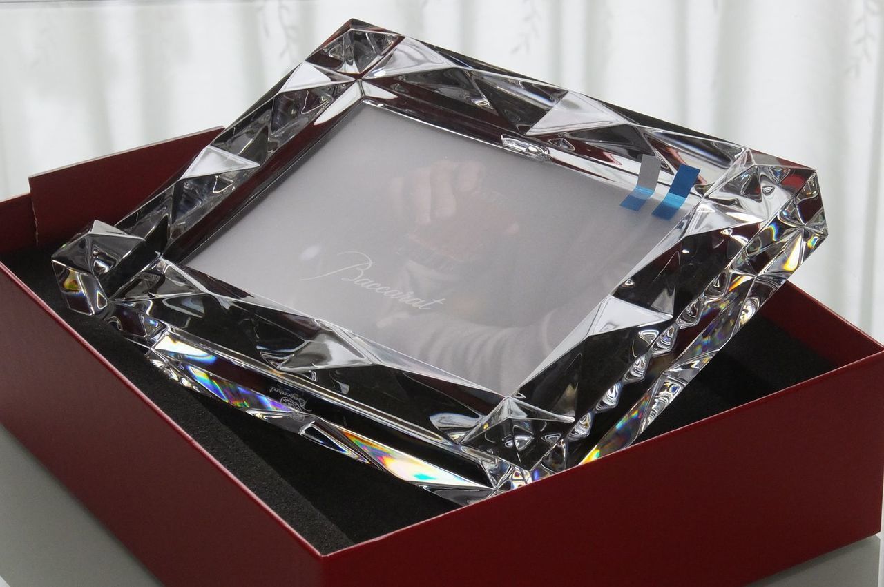 バカラの『ルクソール』フォトフレームが、ブランドを象徴する鮮やかなレッドボックスに収められた写真。ピラミッドのような多面的なカッティングを施したクリスタルが光を捉えて宝石のように輝き、赤い箱とのコントラストが特別な高級感を演出する、最高級の法人ギフトや人生の節目を祝う贈り物としてのイメージ。